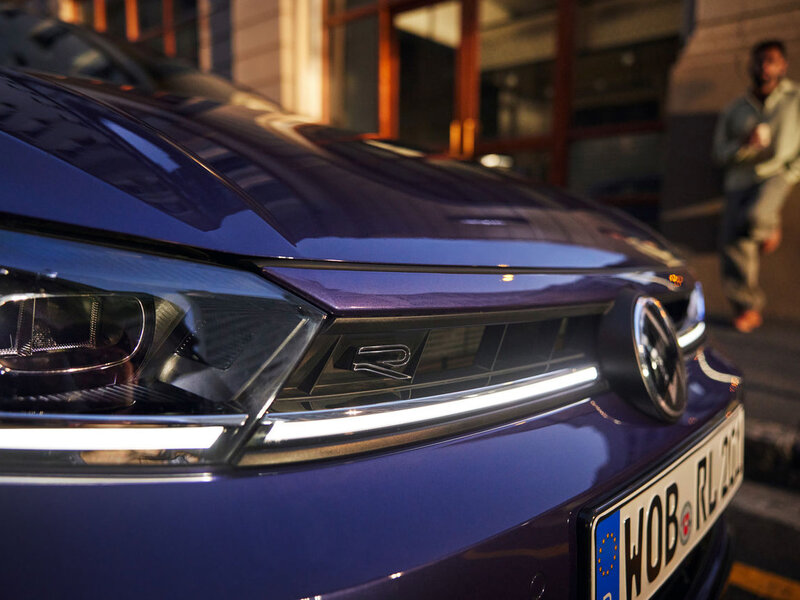 Frontansicht eines blauen Volkswagen Polo mit LED-Scheinwerfern bei urbaner Umgebung in den Abendstunden.