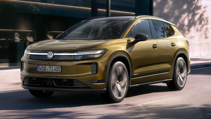 Olivgrüner Volkswagen ID. Tiguan in Dreiviertelansicht bei der Fahrt auf einer Straße vor einem modernen Gebäude