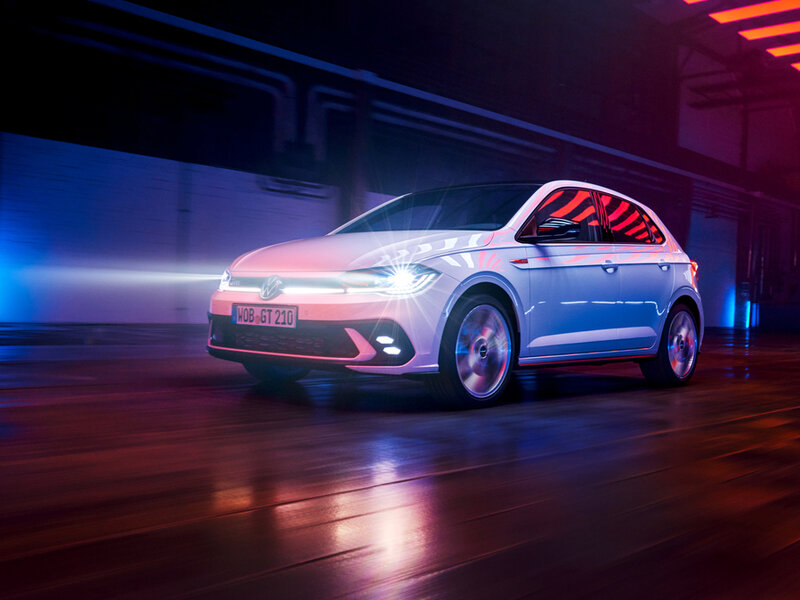 Ein Volkswagen Polo GTI fährt dynamisch durch eine beleuchtete urbane Umgebung bei Nacht.