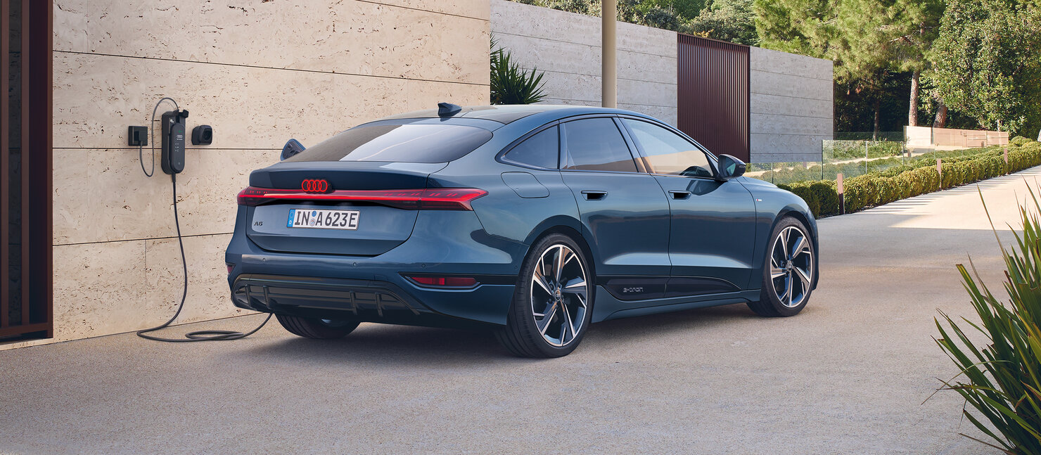 Audi A6 Sportback e-tron an einer Ladesäule, klare Heckgrafik mit durchgehendem Leuchtenband und sportlicher Silhouette