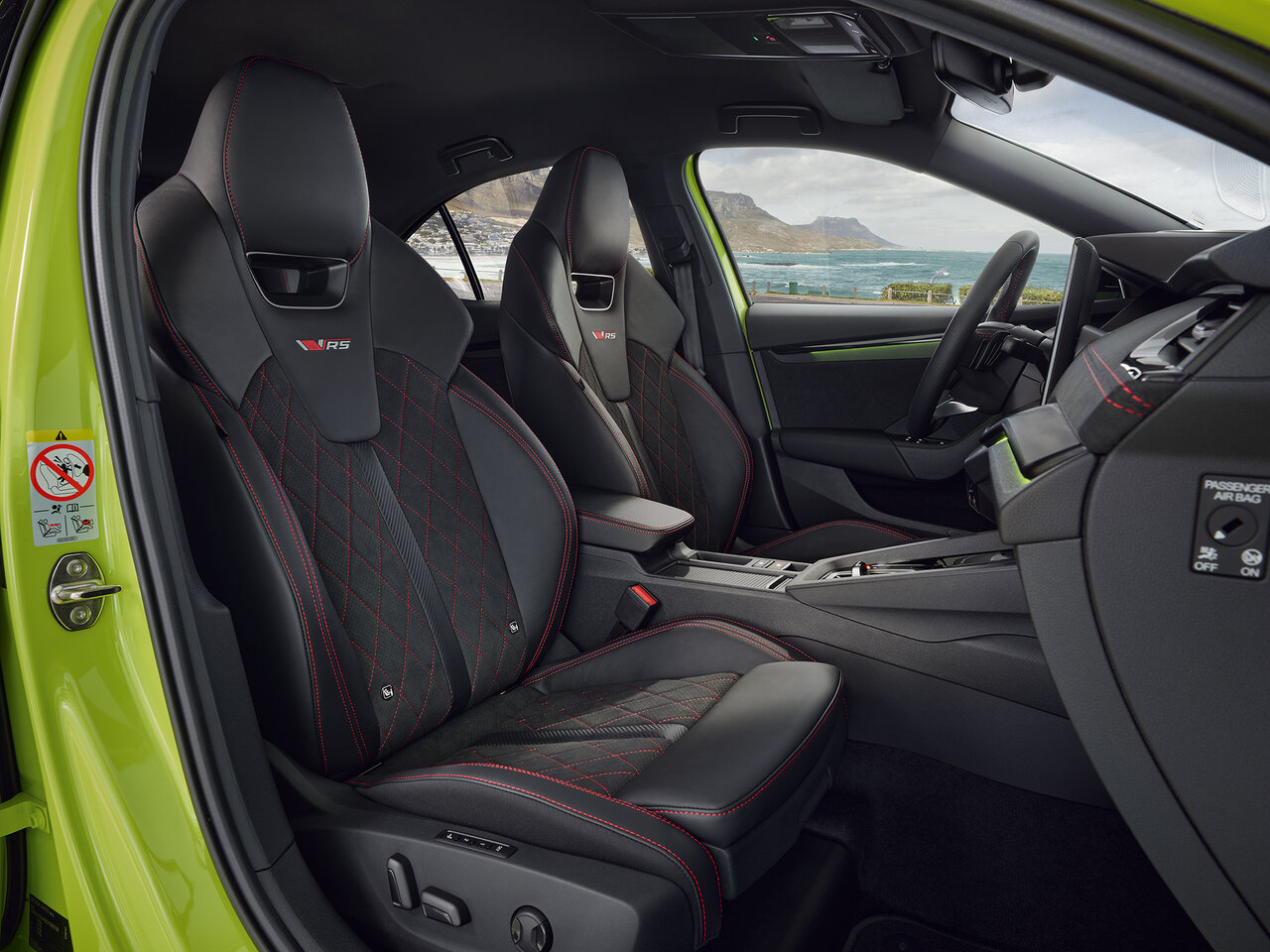 Vordersitze des Škoda Octavia RS Combi in Mamba-Grün mit schwarzen Sportsitzen und roten Ziernähten vor Küstenlandschaft
