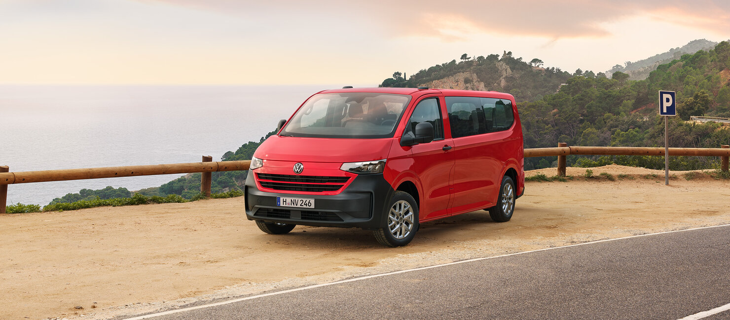 Roter Volkswagen Caravelle steht an Küstenstraße mit Blick aufs Meer bei Abendlicht.