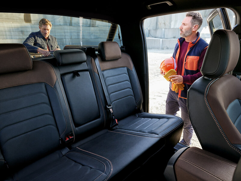 Blick aus dem Fahrzeuginnenraum auf die Rücksitze, während zwei Personen außerhalb des Autos durch die Fenster sichtbar sind.