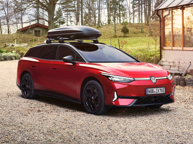 Roter VW ID.7 GTX Tourer mit Dachbox steht vor ländlichem Haus, sportliches Kombi-Design in natürlicher Umgebung.