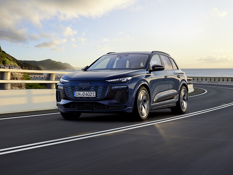 Audi Q6 e-tron fährt auf kurviger Straße mit muskulöser Front, digitalen OLED-Rückleuchten und dynamischem Auftritt