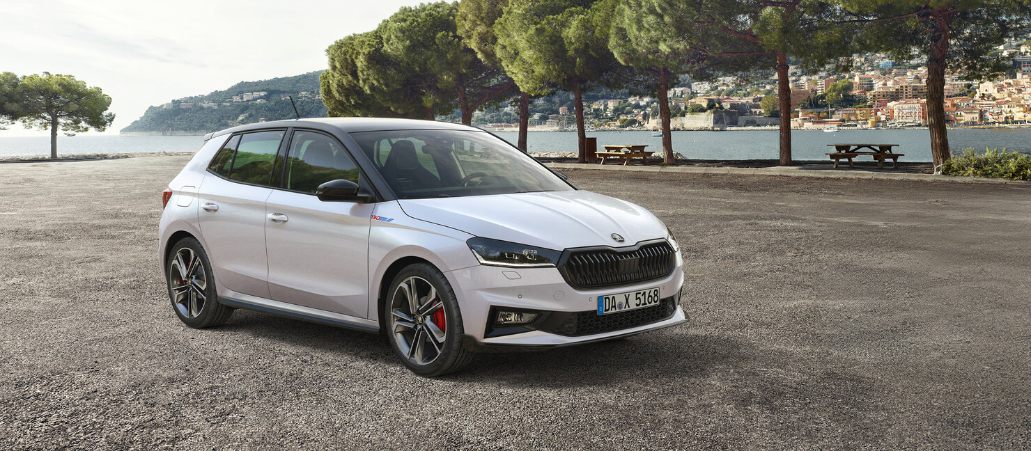 Škoda Fabia 130 Sonderedition in Weiß steht auf einem Parkplatz am Wasser mit Bäumen und Stadt im Hintergrund