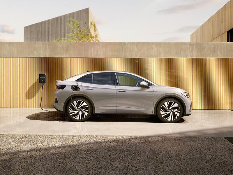 Seitliche Ansicht eines grauen Volkswagen ID.5 vor moderner Architektur mit Holzfassade, geparkt auf einer befestigten Fläche.