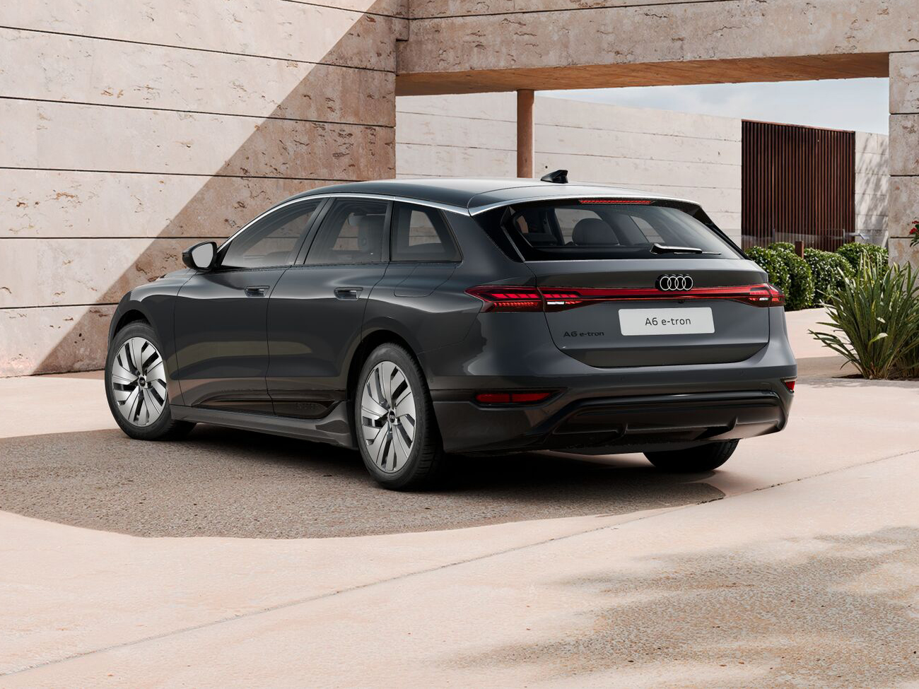 Audi A6 Avant e-tron in Grau in Heckansicht schräg geparkt vor moderner moderner Architektur mit heller Steinwand