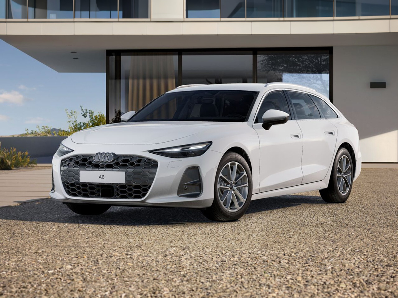 Audi A6 Avant in Front-/ Seitenansicht parkt vor moderner Wohnhausarchitektur mit großer Glasfassade auf gepflasterter Einfahrt