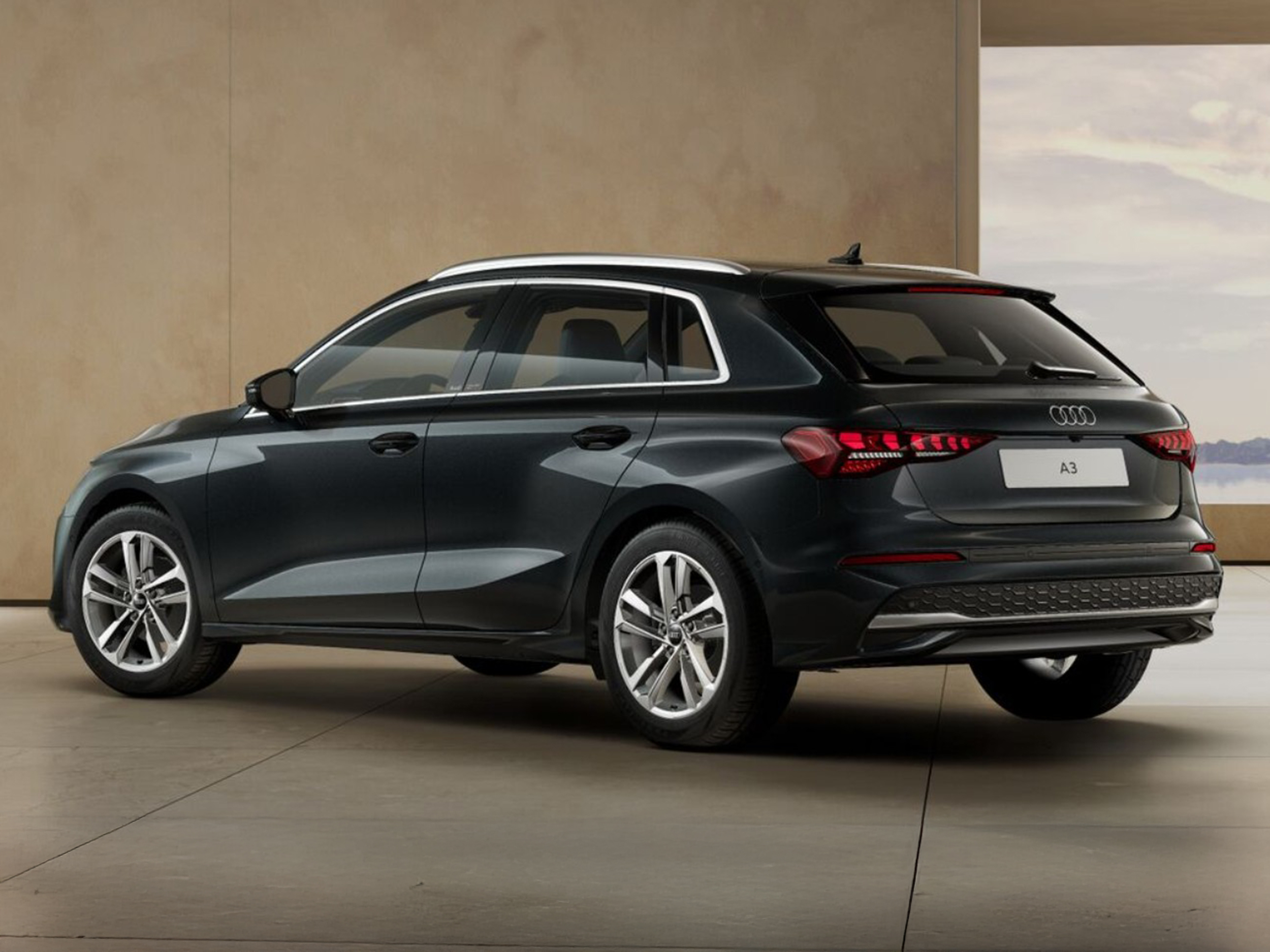 Dunkelgrauer Audi A3 Sportback in Heckansicht steht in modernem Innenraum mit Blick auf eine Landschaft