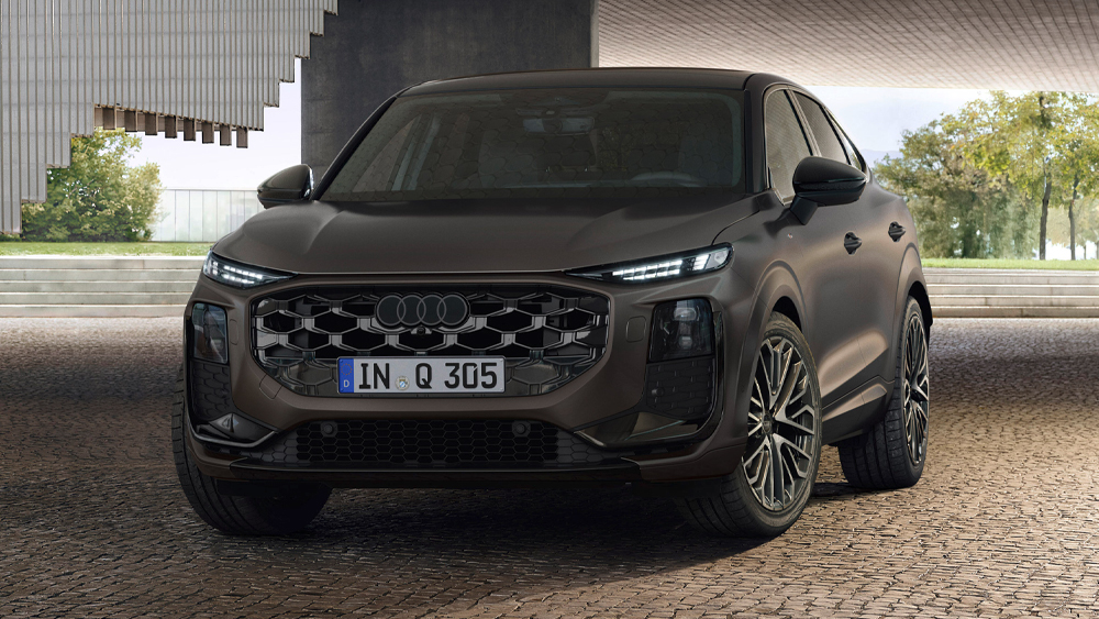 Audi Q3 Sportback in dunkler Lackierung, frontal schräg stehend auf gepflasterter Fläche vor moderner Architektur