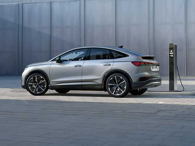 Audi Q4 Sportback e-tron seitlich an Ladesäule vor moderner Architektur mit fließender Coupé-Silhouette