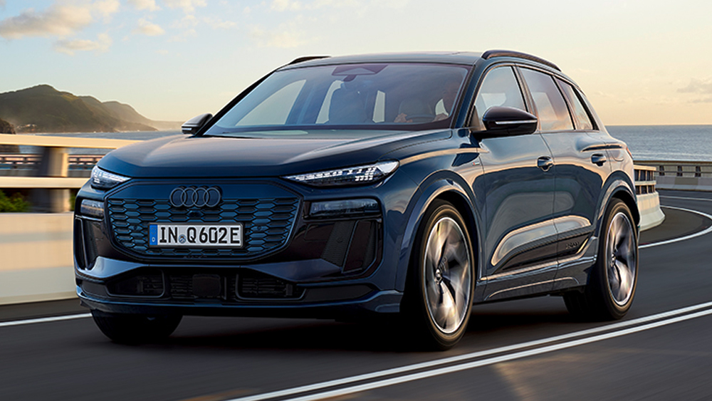 Audi Q6 e-tron in Blau fährt auf Küstenstraße, moderne SUV-Form, markante LED-Lichtsignatur und breiter Singleframe-Grill