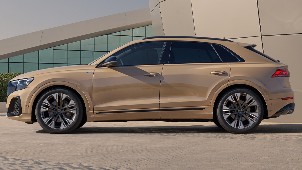 Audi Q8 in Sandmetallic in Seitenansicht vor moderner Architektur, markantes SUV-Design mit großen Leichtmetallrädern