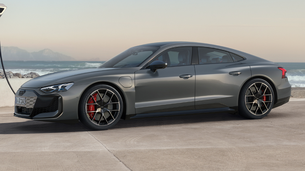 Audi RS e-tron GT in Metallicgrau in dynamischer Seitenansicht auf offener Fläche, markante Räder und sportliche GT-Silhouette im Fokus