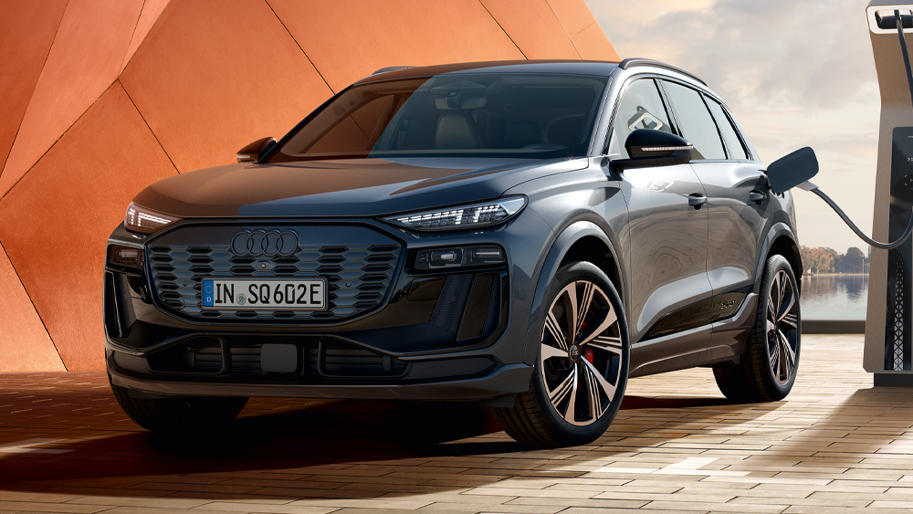 Audi SQ6 e-tron steht an einer Schnellladestation vor moderner Architektur und zeigt sportliches Elektro-SUV-Design