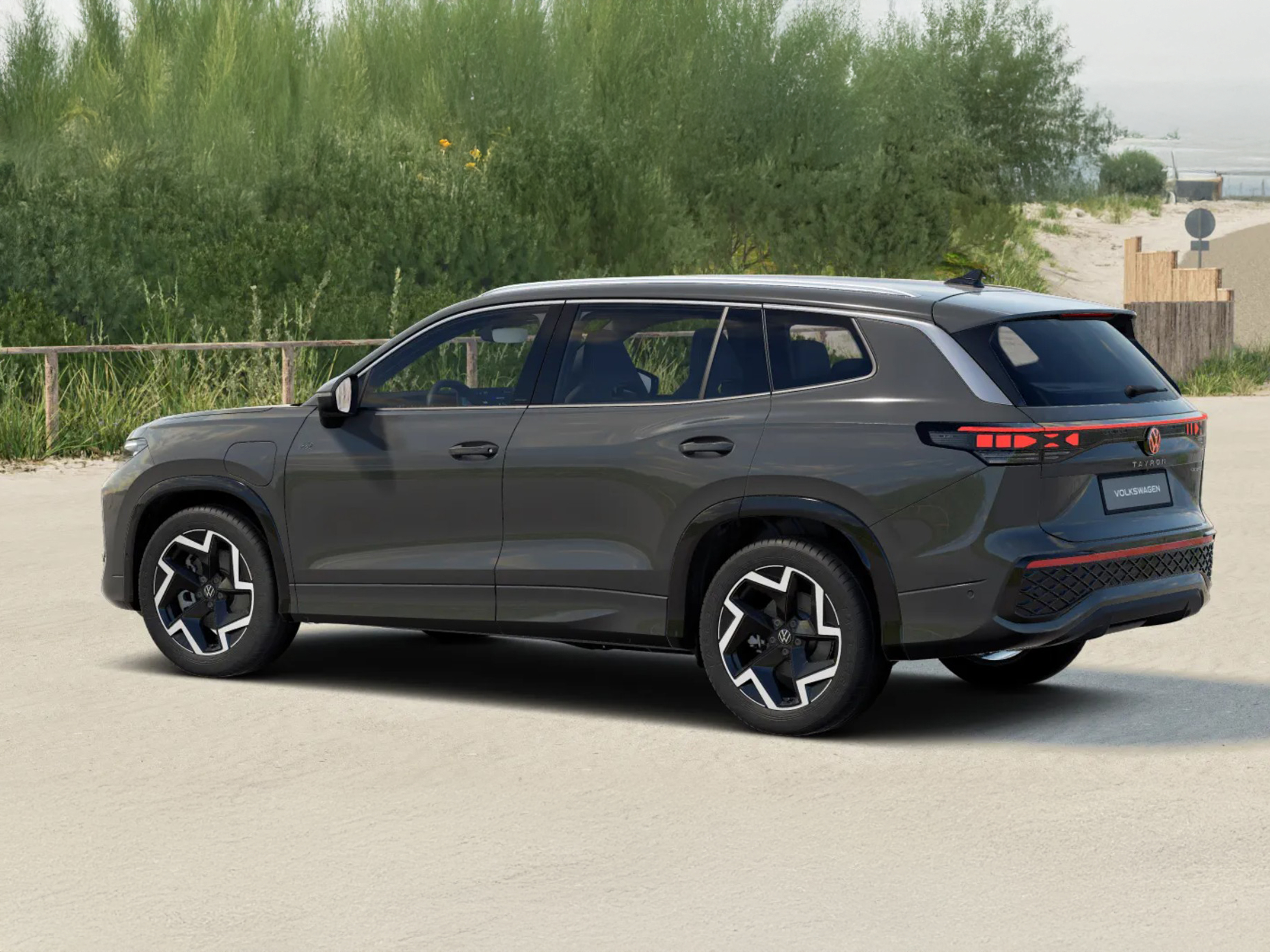 Volkswagen Tayron in Grau aus schräger Heckansicht steht auf einem sandigen Parkplatz nahe der Küste