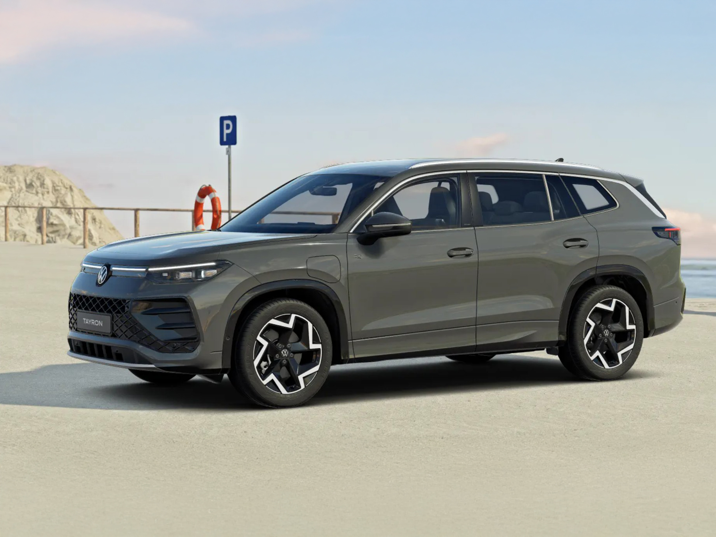 Volkswagen Tayron in Grau steht auf einem Parkplatz nahe der Küste bei klarem Himmel