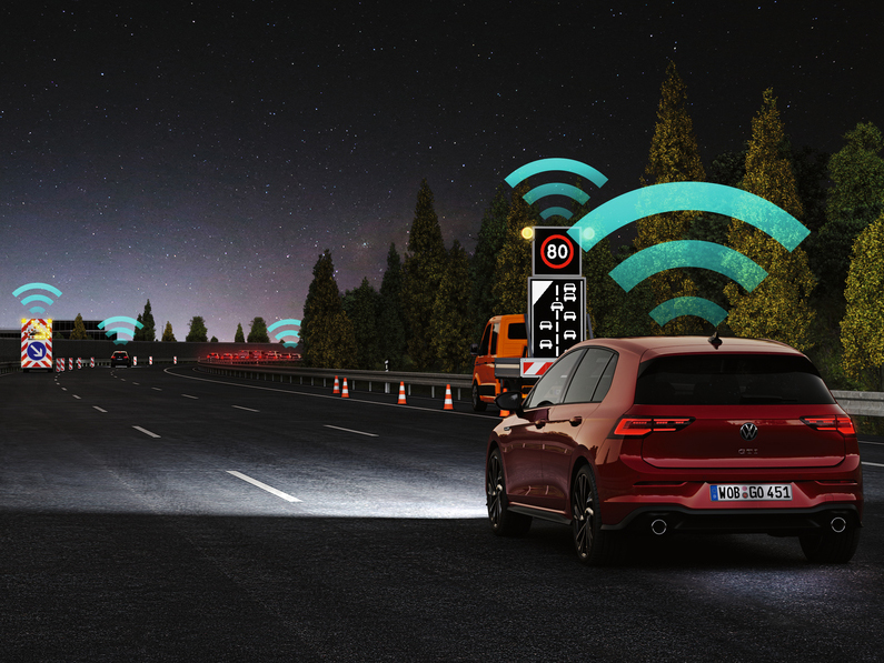 Ein Volkswagen Golf fährt bei Nacht auf einer Straße; grafische Symbole visualisieren aktive Assistenz- und Vernetzungssysteme.