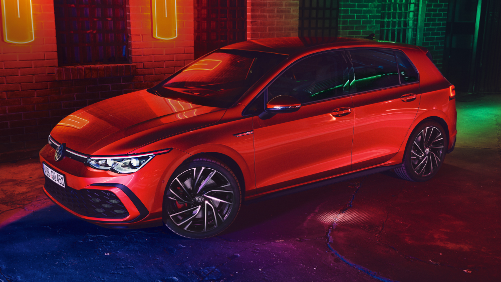 Volkswagen Golf GTI in Rot steht vor einer Backsteinwand mit bunter Neonbeleuchtung