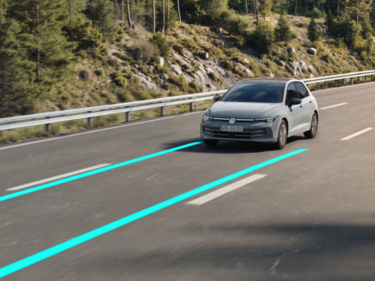 Ein Volkswagen Golf fährt auf einer Landstraße; farbige Linien auf der Fahrbahn visualisieren aktive Fahrassistenzsysteme.