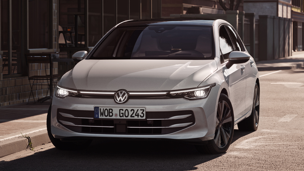 Volkswagen Golf in Weiß steht am Straßenrand bei Tageslicht vor moderner Architektur