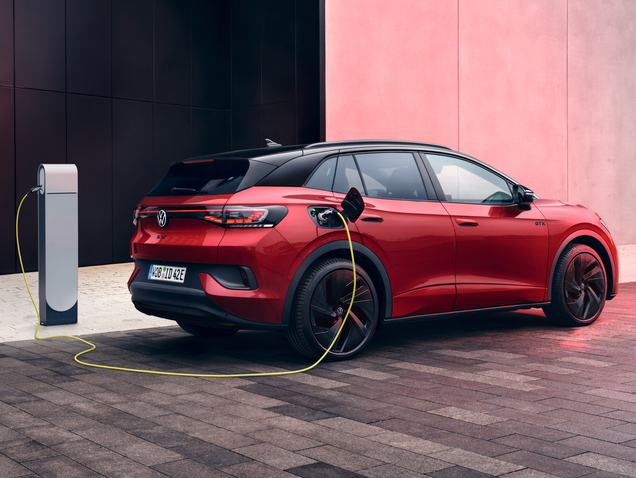Roter Volkswagen ID.4 GTX steht an einer Ladesäule und wird elektrisch geladen, dargestellt aus schräger Seitenansicht vor modernem Gebäude.