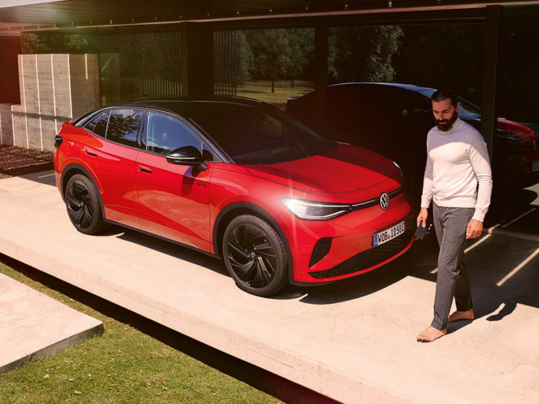 Roter VW ID.5 GTX steht vor einem modernen Haus, ein Mann geht am Fahrzeug vorbei; sportliches Elektro-SUV mit Allradantrieb im Außenbereich.