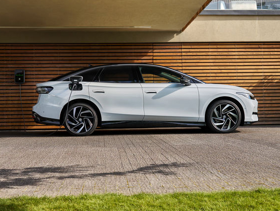 Weißer Volkswagen ID.7 steht vor einem modernen Haus und ist über ein Ladekabel mit einer Wallbox verbunden.