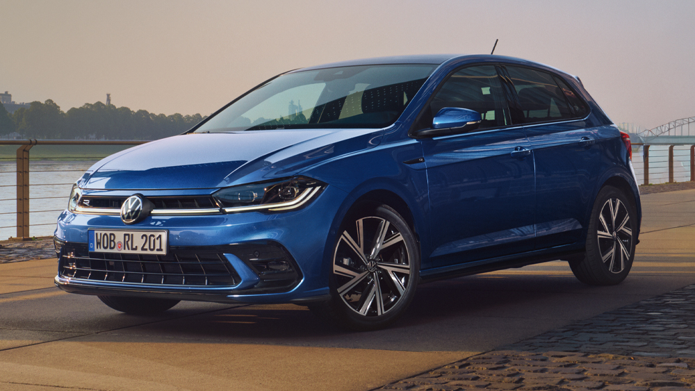 Volkswagen Polo in Blau steht auf einer Promenade mit Blick auf einen Fluss und eine Brücke