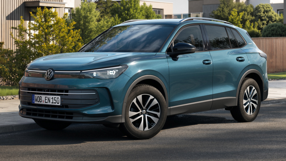 Volkswagen Tiguan in Petrolblau, Front-Dreiviertelansicht, geparkt in moderner Wohnstraße mit Grünflächen