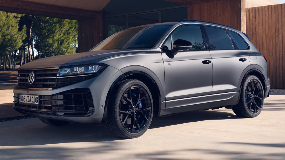 Grauer Volkswagen Touareg R eHybrid mit schwarzen Leichtmetallrädern, geparkt vor moderner Architektur, sportlich-elegante Seitenansicht