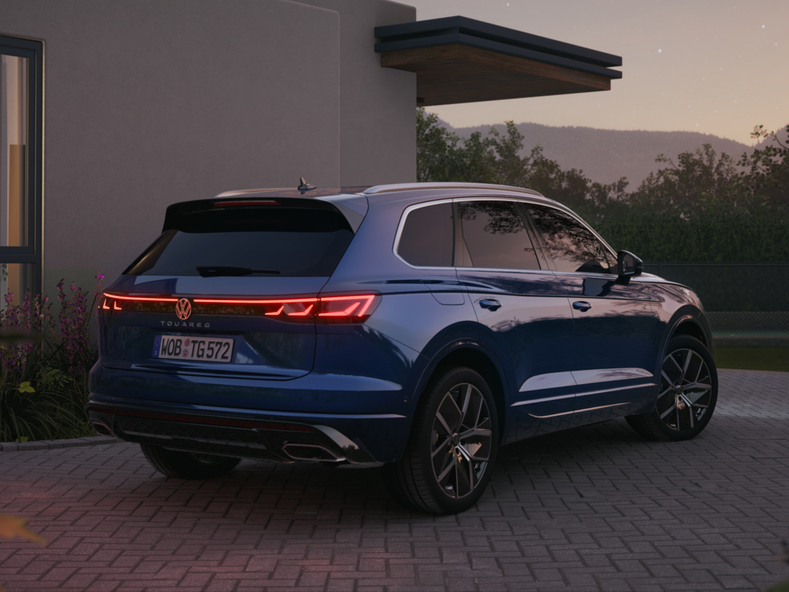 Heckansicht eines blauen Volkswagen Touareg vor einem modernen Wohnhaus bei Abendlicht.