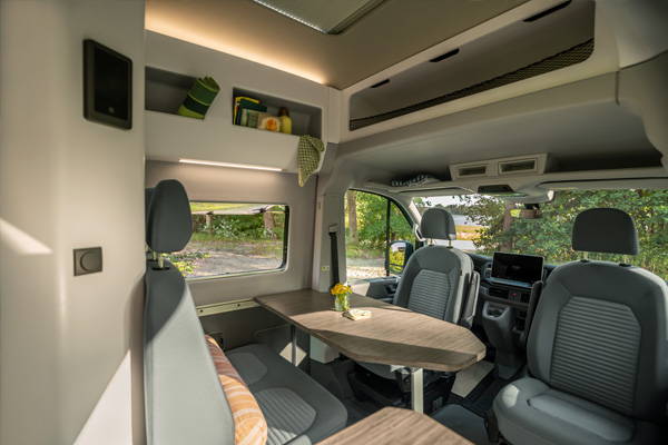 Innenraum des Volkswagen Grand California mit Sitzgruppe, drehbaren Vordersitzen, Tisch und integrierter Küchenzeile bei Tageslicht