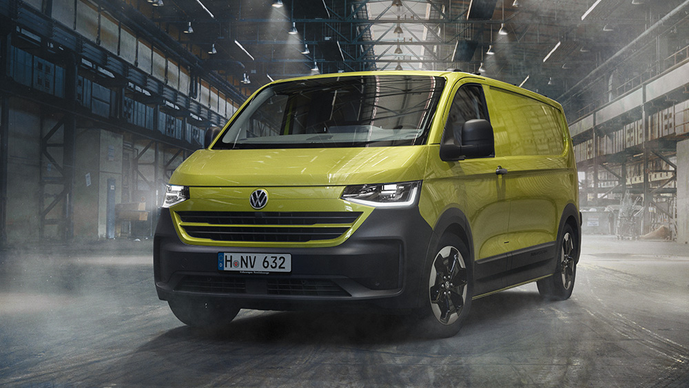 Grüner Volkswagen Transporter steht in Industriehalle, Licht fällt durch Fenster, feuchte Bodenfläche.